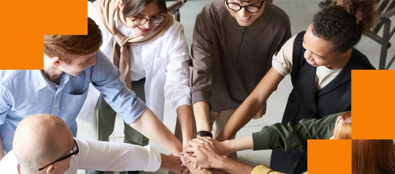 Diverse group of students and professionals putting their hands together in a team huddle, representing collaboration and unity in the Risers community